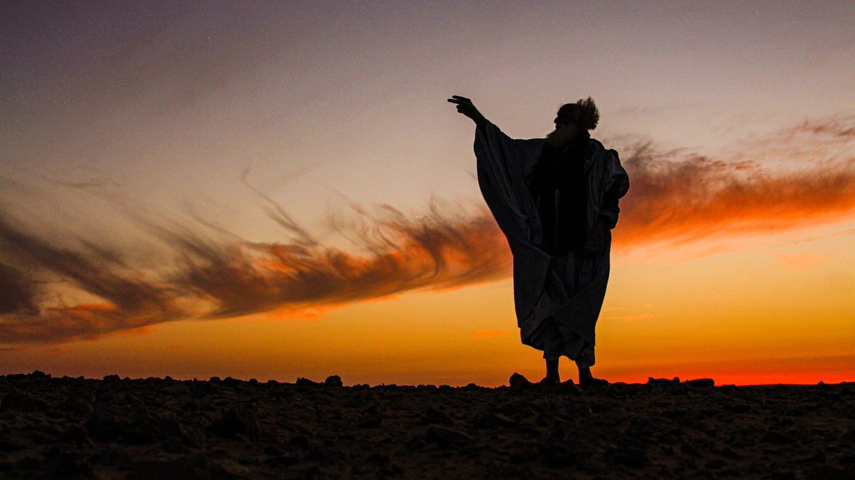 A dramatic silhouette of a person in the desert against a vibrant sunset sky.